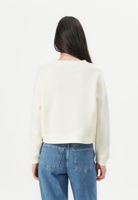 White, cropped sweatshirt with a wide neckline and long sleeves, paired with light blue high-waisted jeans featuring back pockets.
