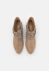 Vaaleanruskeat mokkasaappaat, joissa koristeelliset leikkaukset, niittikoristeet ja sivuvetoketju sulkemista varten. Sileä sisävuori.