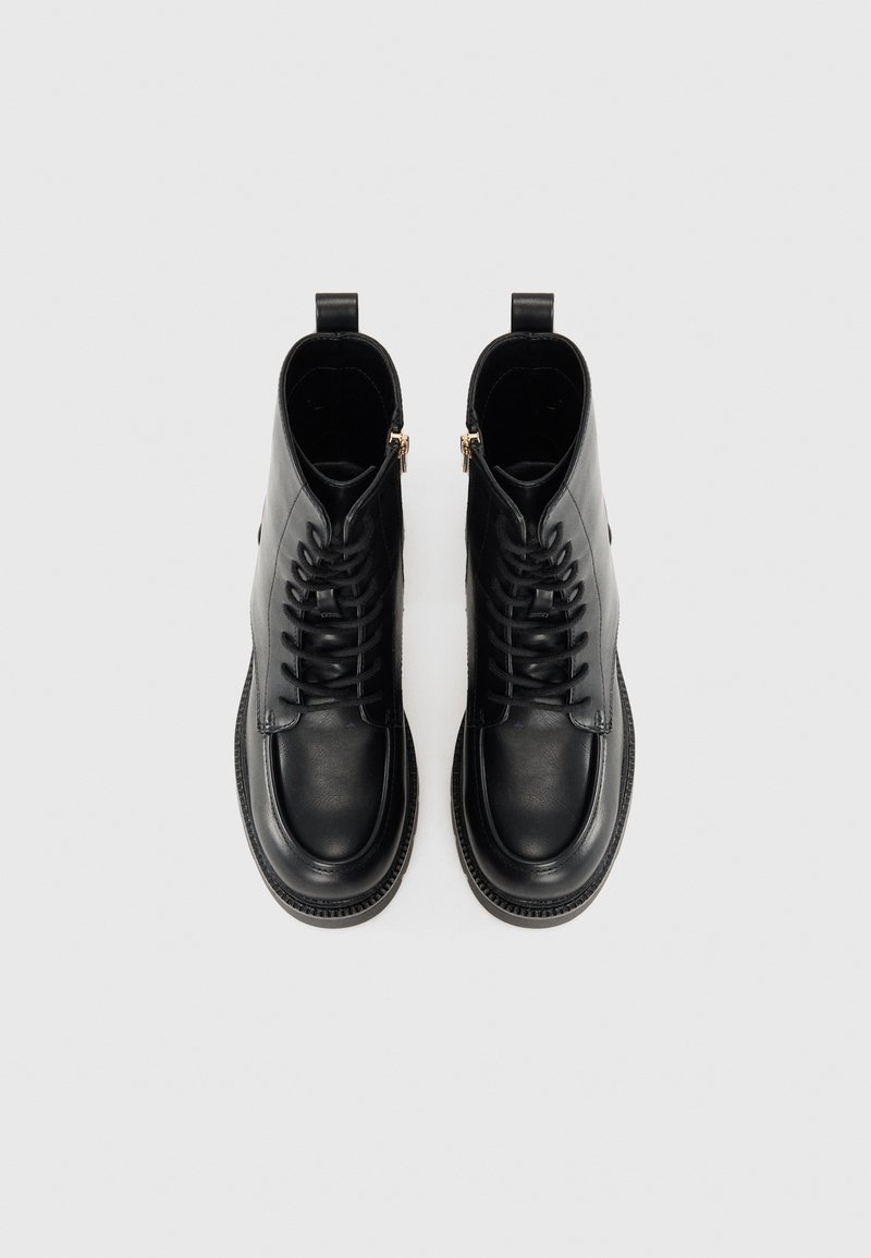 Stivali alla caviglia in pelle nera con finitura liscia, lacci sul davanti, cerniere laterali e suola testurizzata, dotati di punte arrotondate e dettagli a linguetta.