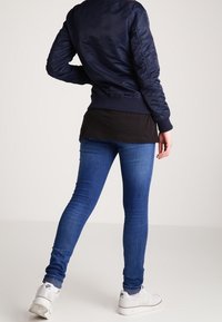 Marinblå bomberjacka med ribbad nederkant, kombinerad med svart lagerpåde topp och blå skinny jeans, avslutad med vita sneakers.