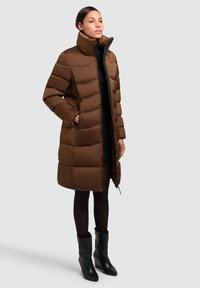 Rjava puhasta bunda z visokim ovratnikom, z zadrgo spredaj, stranskimi žepi in prešitim vzorcem. Nosi se čez črno obleko in je kombinirana s črnimi škornji.