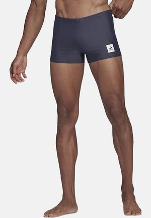 Navy blue swim shorts with a fitted design, made from stretchy material. Features a white Adidas logo on the left leg.