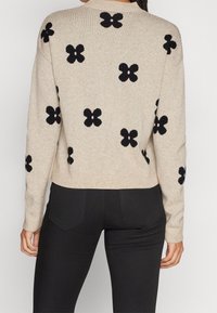 Beiger Strickpullover mit schwarzen Blumenmustern, rundem Ausschnitt und gerippten Bündchen. Einfaches, kurz geschnittenes Design mit lockerer Passform.