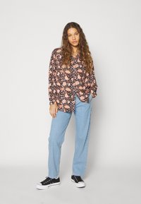 Camisa de botones de flores con mangas largas en negro, rosa y naranja. Combinada con pantalones vaqueros anchos de color azul claro y zapatillas negras.