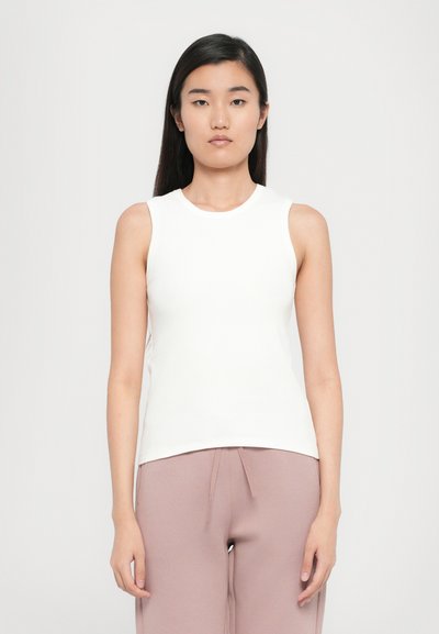 Top sans manches blanc en tissu côtelé. Il présente un col rond et une coupe ajustée. Assorti à un pantalon rose clair à coupe décontractée.