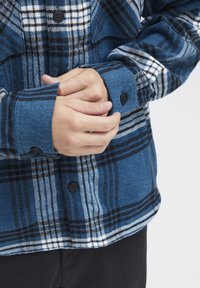 Blauwe en zwarte geblokte flanellen overhemd met een knoopmanchet, gemaakt van een zachte, gestructureerde stof en een opvallend geruit patroon.
