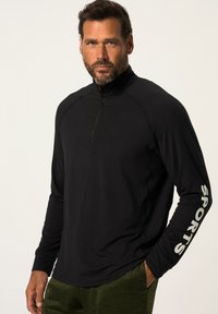 Schwarzes Longsleeve mit Viertelreißverschluss, das "SPORTS" in Weiß den rechten Ärmel entlang bedruckt hat. Weicher, elastischer Stoff mit einer figurbetonten Passform.