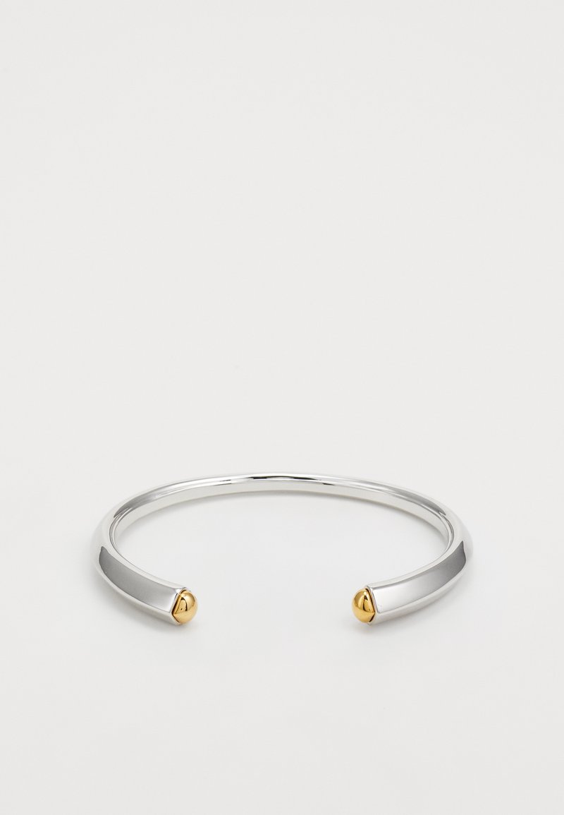 Pulsera de brazalete de metal plateado con acabado suave y pulido, que presenta dos acentos dorados redondeados en los extremos abiertos.