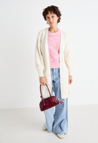Elfenben cardigan med texturerad stickning, rosa prickig tröja, vida blå denimjeans och en liten vinröd handväska. Lätta skor.