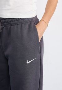 Sivé Nike tepláky s elastickým pásom a šnúrkou. Obsahujú bočné vrecká a malé biele logo Nike na ľavom stehne.