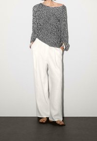 Black and white patterned long-sleeve top with an asymmetrical hem, paired with white wide-leg pants, and simple black sandals. Silver bracelet accent.