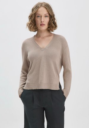 Beige v-hals trui met lange mouwen, geribbelde zoom en subtiele textuur, gecombineerd met donkere hoge tailleschoenen.