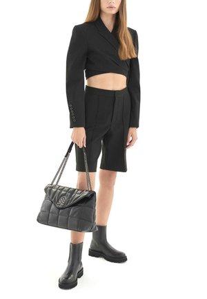 Black cropped blazer with long sleeves, high-waisted black shorts, chunky black ankle boots, and a quilted black handbag with chain strap.