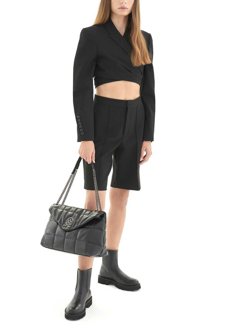 Blazer nero corto con maniche lunghe, pantaloni corti neri a vita alta, stivaletti neri chunky alla caviglia e borsa nera trapuntata con tracolla a catena.
