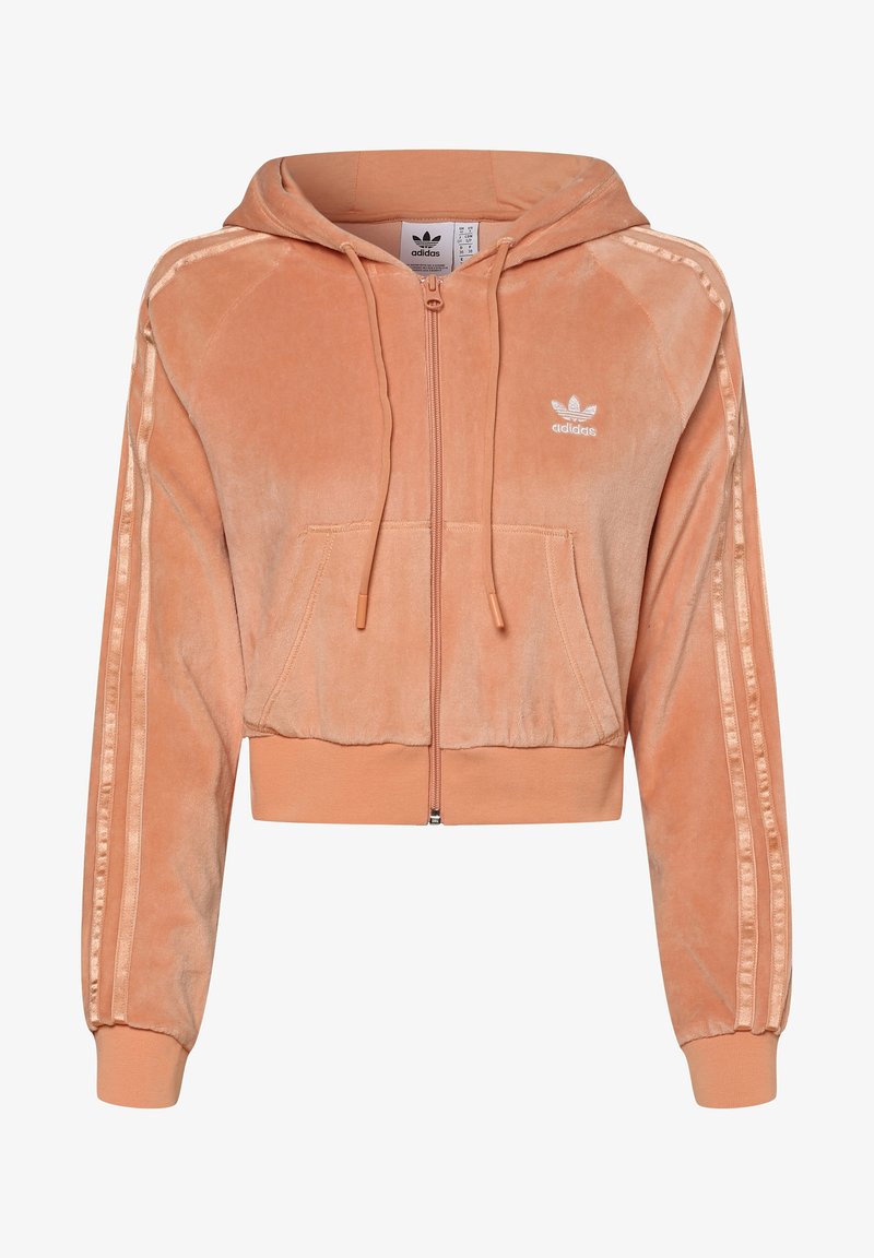 Zkrácená broskvová velurová mikina s předním zipem, šňůrkami, klokaní kapsou a bílým logem Adidas; má žebrované manžety a boční pruhy.