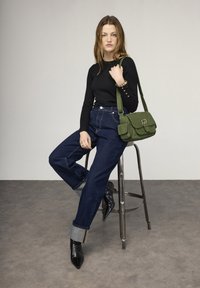 Top nero a maniche lunghe, jeans di denim blu a vita alta con risvolti, tacchi neri con punta a punta e una piccola borsa a tracolla verde.