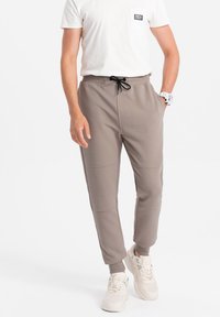 Pánské hnědé jogger kalhoty s ribbed texturou, elastickým pasem a šňůrkou. Úzký střih se bočními kapsami a manžetami na kotnících.