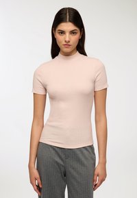 Top a maniche corte a coste in morbido tessuto rosa con scollo alto, design aderente, texture liscia, abbinato a pantaloni grigi a righe sottili.