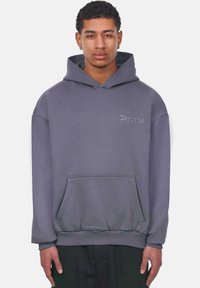 Sudadera gris de tela suave, con un bolsillo frontal, dobladillo y puños acanalados, y texto bordado en el pecho.