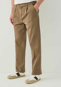 Khaki trousers made of cotton blend, featuring a straight-leg design, two side pockets, and a button closure. Styled with white and grey sneakers.