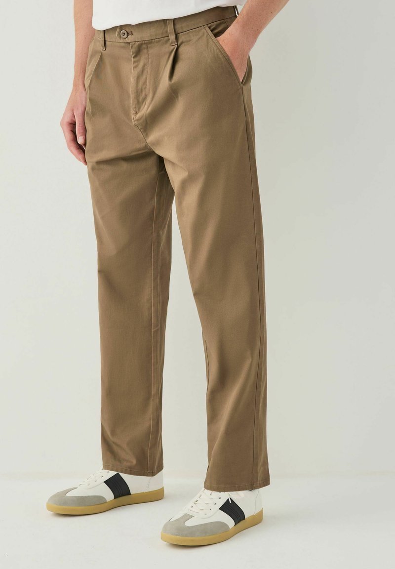 Khaki trousers made of cotton blend, featuring a straight-leg design, two side pockets, and a button closure. Styled with white and grey sneakers.