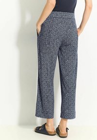 Navy patterned wide-leg pants with a floral design, two side pockets, and a smooth texture, paired with dark slip-on sandals.