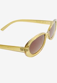 Geltonos spalvos ovalios formos akiniai nuo saulės su skaidraus plastiko rėmeliu ir išlenktais šonais, kuriuose yra išgraviruotas tekstas.