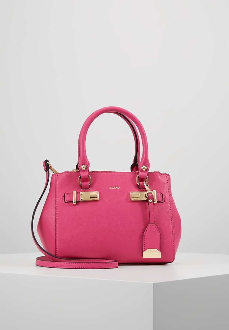 Sac à main en cuir rose vif avec doubles poignées, ferrures dorées, bandoulière amovible et étiquette de marque sur une surface blanche.