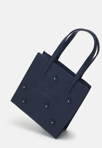 Laavinsininen olkalaukku, jossa on kohopainettuja kukkakuvioita, hopeisia niittejä ja etupuolella teksti "EST 1988 TED BAKER". Teksturoidusta materiaalista ja kaksoiskahvoilla varustettu.