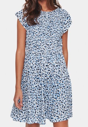 Mujer vistiendo un vestido de manga corta con un estampado abstracto en azul, negro y blanco, con un corpiño fruncido y una falda acampanada, sobre un fondo liso.