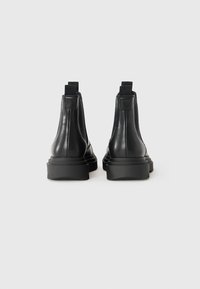 Pair of black leather ankle boots with thick rubber soles and fabric pull tabs, shown from the back against a white background.