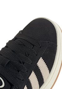 Baskets en daim noir avec une tige texturée, dotées de trois bandes beiges, d'un embout arrondi, de lacets noirs et d'une semelle en caoutchouc blanche.