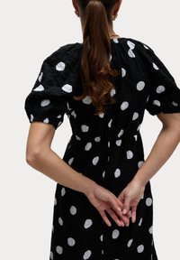 Schwarzes Kleid mit weißen Punkten, Puffärmeln und geraffter Taille. Besitzt einen strukturierten, zerknitterten Stoff und eine lässige Passform.