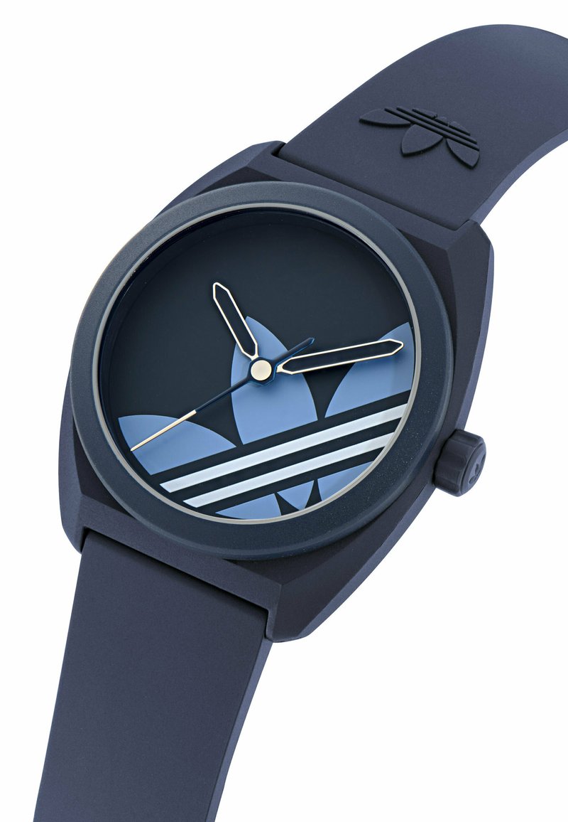 Montre-bracelet Adidas bleu foncé avec trois bandes blanches et logo trèfle sur le cadran, bracelet en silicone assorti, et aiguilles lumineuses indiquant 10h10.
