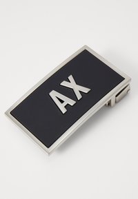 Μεταλλική αγκράφα ζώνης σε ορθογώνιο σχήμα, με το ασημένιο λογότυπο "AX" σε μαύρο ματ φόντο και γυαλιστερή ασημένια κορνίζα.