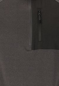 Grå jumper med en fjärdedels dragkedja och en liten dragkedjeficka på bröstet. Texturerad tyg med en slät övre del.