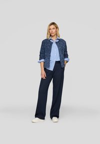 Navy textured cardigan over a light blue striped shirt, paired with dark pinstriped wide-leg pants and white shoes. Simple, casual outfit.