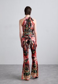 Combinaison à col halter avec un motif abstrait coloré en rouge, vert et jaune, des jambes évasées et un lien dans le dos.
