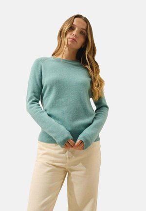 Pull en tricot teal clair avec des poignets et un ourlet côtelés, design col rond, et texture douce, associé à un pantalon beige clair.