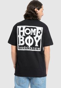 Schwarzes Baumwoll-T-Shirt mit einem großen weißen Grafikdruck auf der Rückseite, der den Text "HOME BOY loud.couture" in einer kräftigen, blockartigen Schriftart zeigt.
