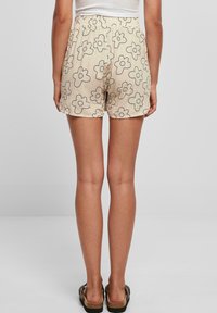 Šviesiai rudos šortai su juodais gėlėtais raštais, elastinga juosta ir laisvas siluetas. Audinys atrodo lengvas ir lygus, turintis kasdienį dizainą.