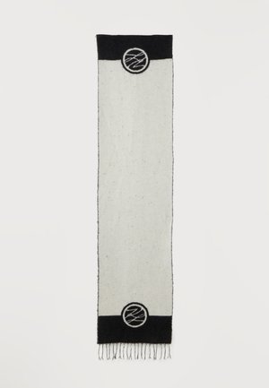 Longue écharpe rectangulaire blanche avec extrémités noires, chaque extrémité présentant un emblème circulaire avec un motif abstrait en lignes et des franges en bas.