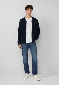 Marineblauer, gerippter Cardigan über einem weißen T-Shirt, kombiniert mit blauen Jeans und weißen Turnschuhen. Der Cardigan hat eine lockere Passform und einen offenen Vorderteil.