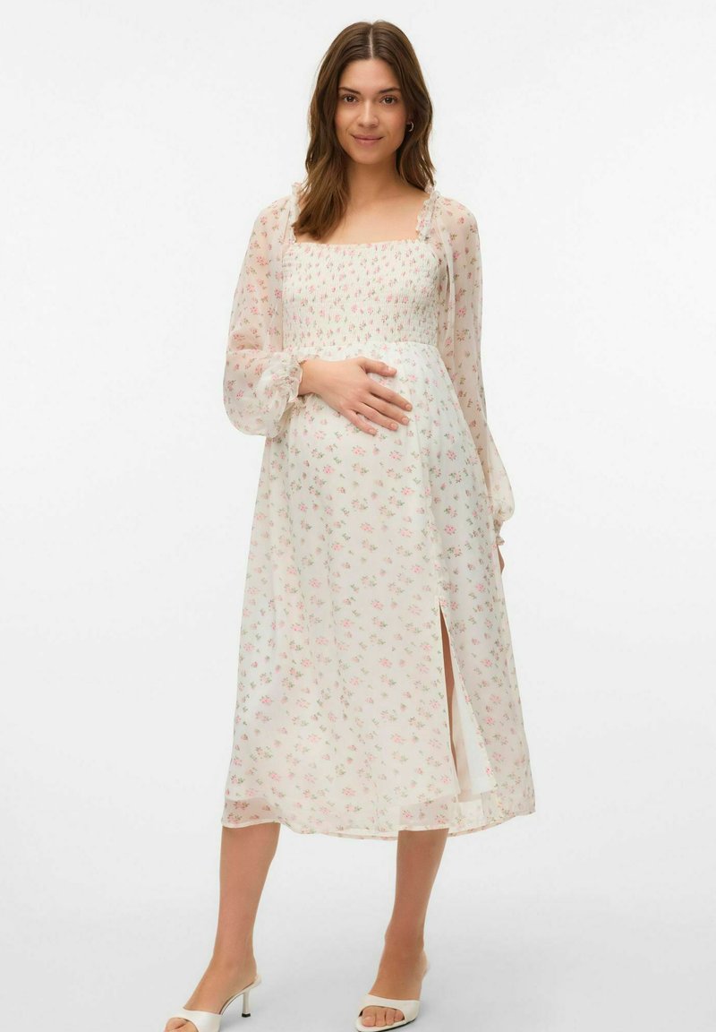 Robe midi florale en tissu transparent, présentant un corsage froncé, de longues manches bouffantes et une fente sur le côté. Les couleurs incluent le rose clair et la crème.