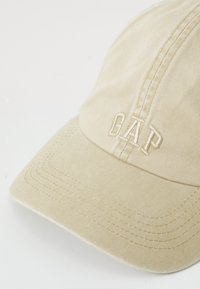 Beige színű pamut baseball sapka, amelynek elején a "GAP" hímezve van, ívelt karimával és látható varrásokkal.