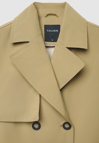 Beiger Trenchcoat mit weitem Kragen, doppelreihigen Knöpfen und einem Etikett mit der Aufschrift "CALLIOPE" auf der Innenseite. Glatter, maßgeschneiderter Stoff.