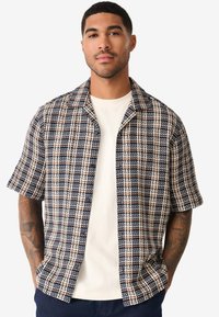 Chemise à manches courtes à carreaux bleu marine et crème, en tissu texturé, avec un col à revers et une fermeture à boutons à l'avant.