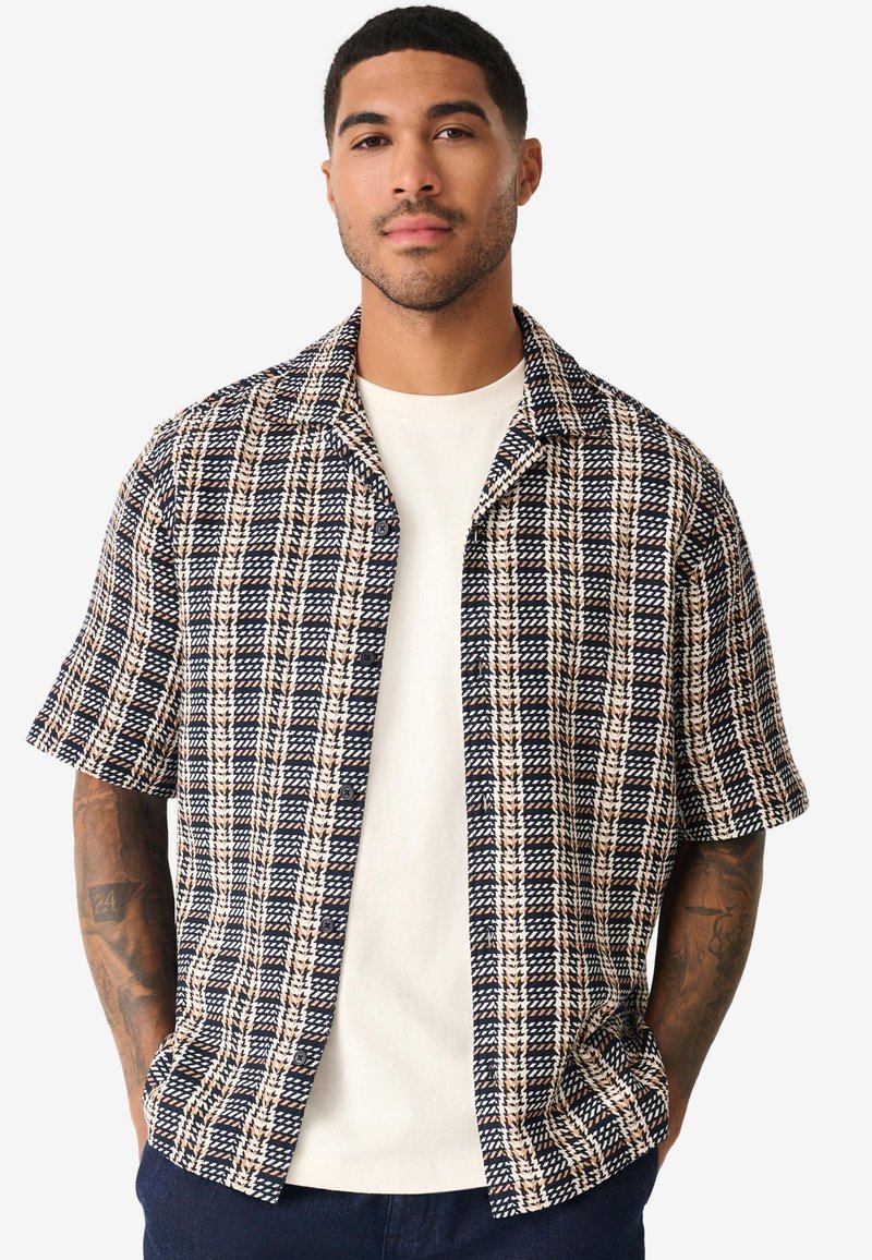 Chemise à manches courtes à carreaux bleu marine et crème, en tissu texturé, avec un col à revers et une fermeture à boutons à l'avant.