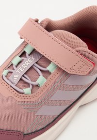 Chaussure de sport rose avec tige en mesh respirant, sangle réglable, lacets colorés et semelle en caoutchouc texturé. Présente un logo sur le côté.