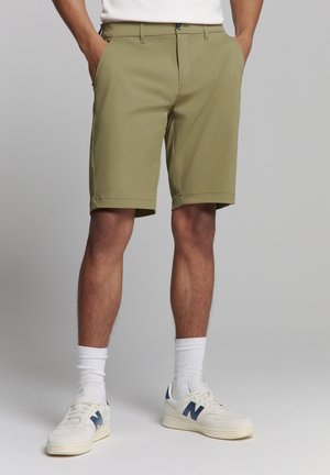 Olijfgroene shorts met een vlakke voorkant, twee zijzakken en een klassieke pasvorm. Gecombineerd met witte hoge sneakers en crew-sokken.